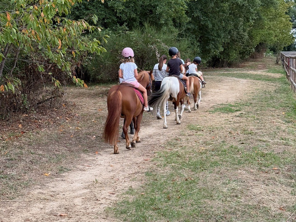 Groupe de jeunes cavaliers en balade à poney sur un chemin bordé d'arbres, au Centre Équestre de Venat